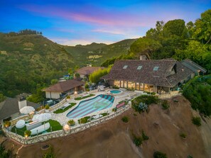 Une grande maison avec une piscine, entourée de collines et d’arbres.