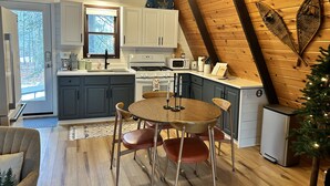 A cozy kitchen with wooden walls, a dining table, and modern appliances. - MCM A-frame: HOT TUB; Lake; Fall Colors; Fireplace; Nature; Cozy; Kayaks (Johannesburg)