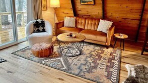 A cozy room with a wooden interior, a sofa, a chair, a small table, and a rug. - MCM A-frame: HOT TUB; Lake; Fall Colors; Fireplace; Nature; Cozy; Kayaks (Johannesburg)
