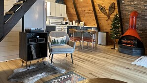 A cozy loft-style living space with a wooden ceiling, a fireplace, a dining area, and a kitchen. - MCM A-frame: HOT TUB; Lake; Fall Colors; Fireplace; Nature; Cozy; Kayaks (Johannesburg)