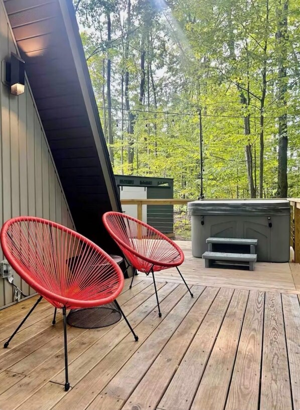 Une terrasse en bois avec deux chaises rouges et un jacuzzi.