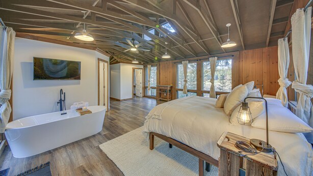 A spacious bedroom with a large bed, a modern bathtub, and a wooden ceiling. - Bonners Ferry Cabin w/ Wraparound Deck & Views! (Bonners Ferry)