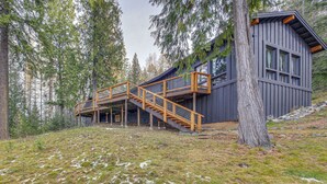 A cabin with a wooden staircase leading to a deck, surrounded by tall trees. - Bonners Ferry Cabin w/ Wraparound Deck & Views! (Bonners Ferry)