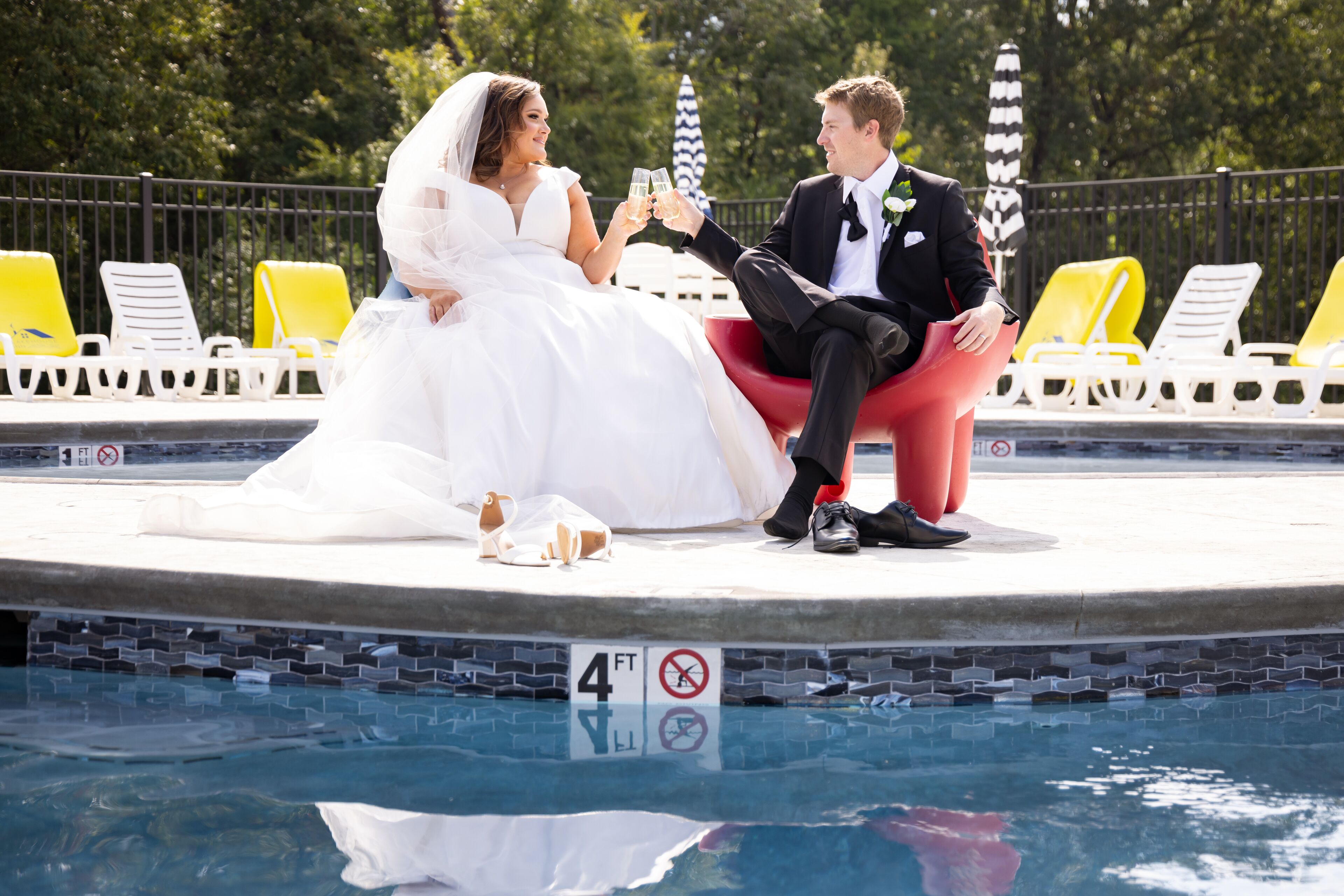 Una pareja brindando junto a una piscina con un letrero que indica una profundidad de 1.2 metros.