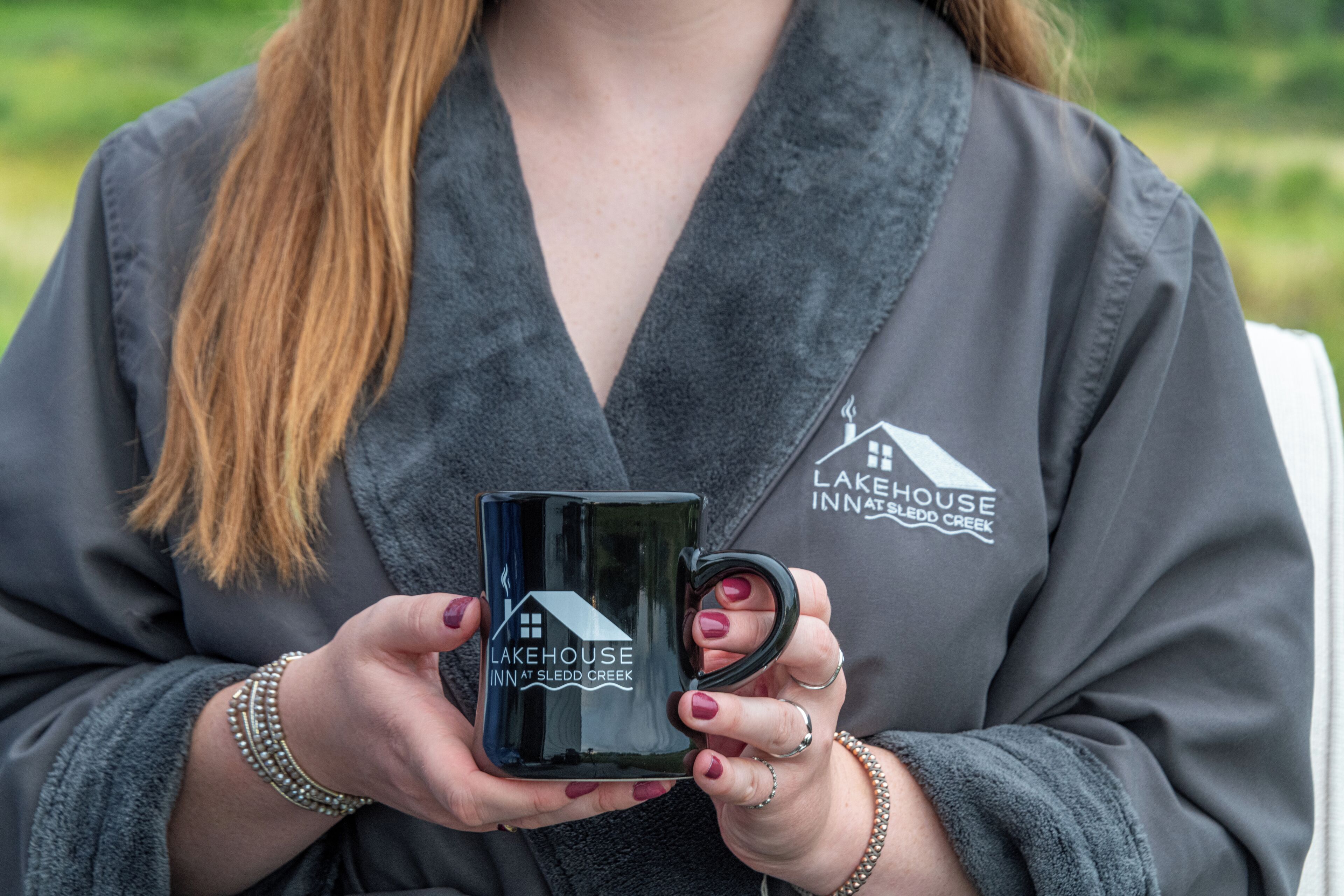 Eine Person hält eine schwarze Tasse mit dem Schriftzug 'Lakehouse Inn at Sledd Creek'.