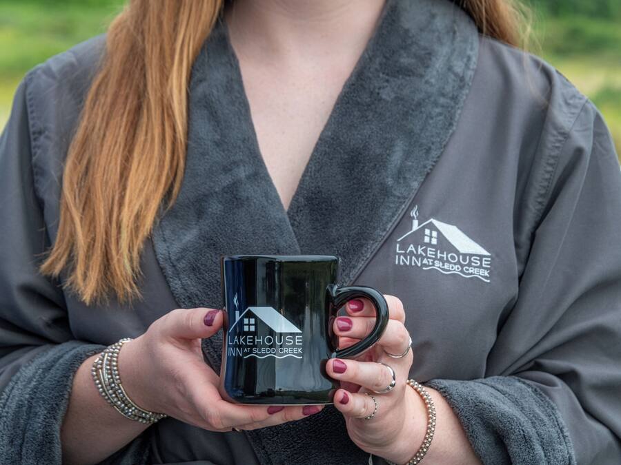 Eine Person hält eine schwarze Tasse mit dem Schriftzug 'Lakehouse Inn at Sledd Creek'.