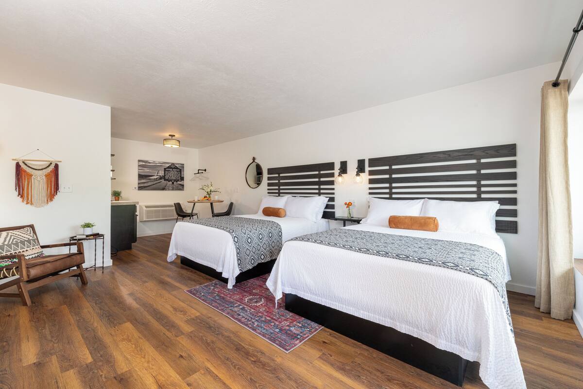 Ein Hotelzimmer mit zwei Betten, Holzboden, Schreibtisch mit Stuhl und einem Wandspiegel.