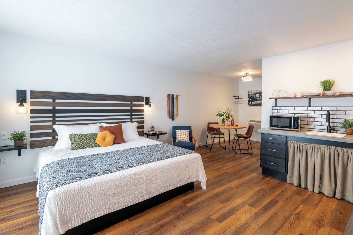 Ein modernes Hotelzimmer mit einem großen Bett, einer Küchenzeile, einem Essbereich und einem kleinen Tisch mit Stühlen.