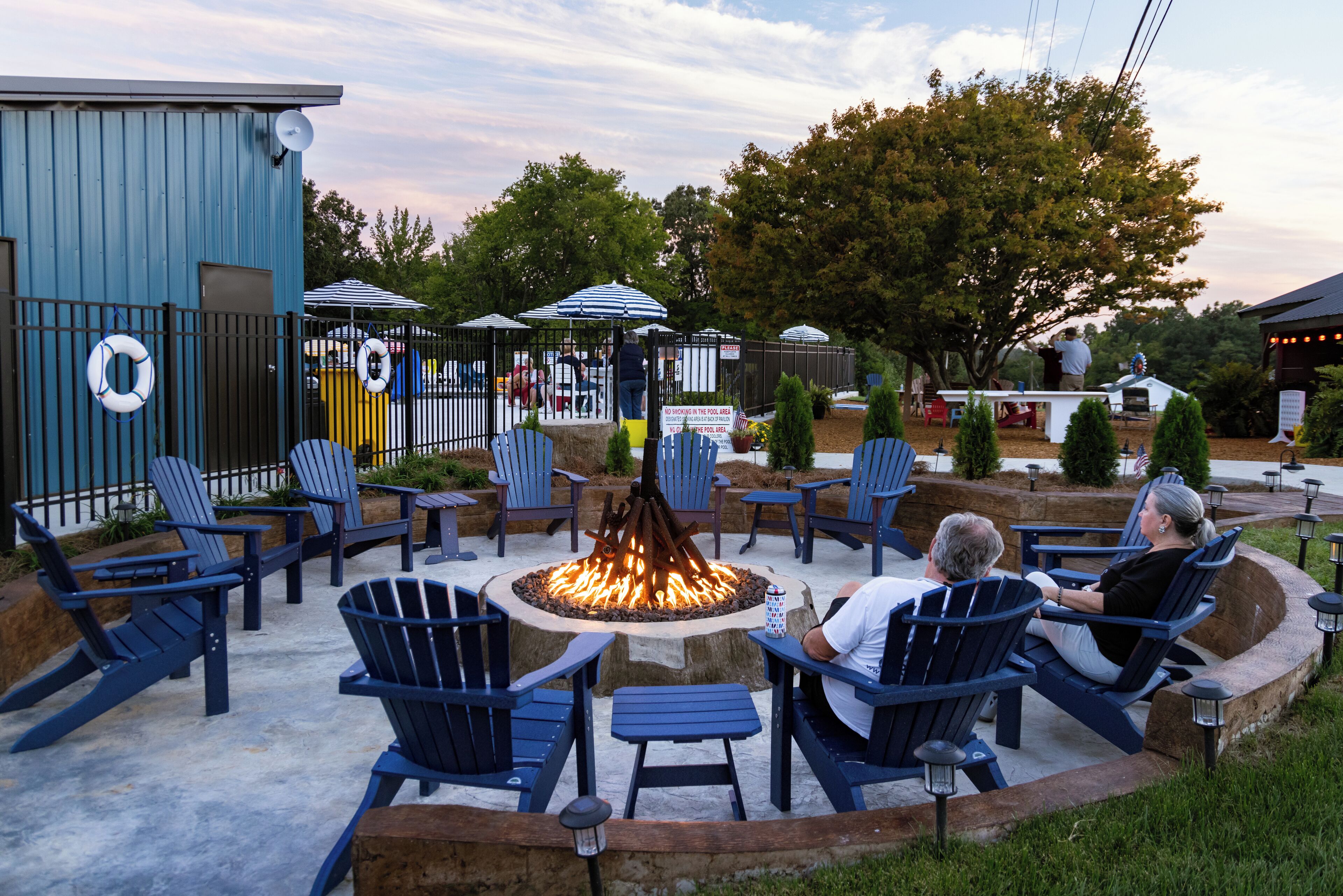 An outdoor seating area with blue Adirondack chairs arranged around a central fire pit.