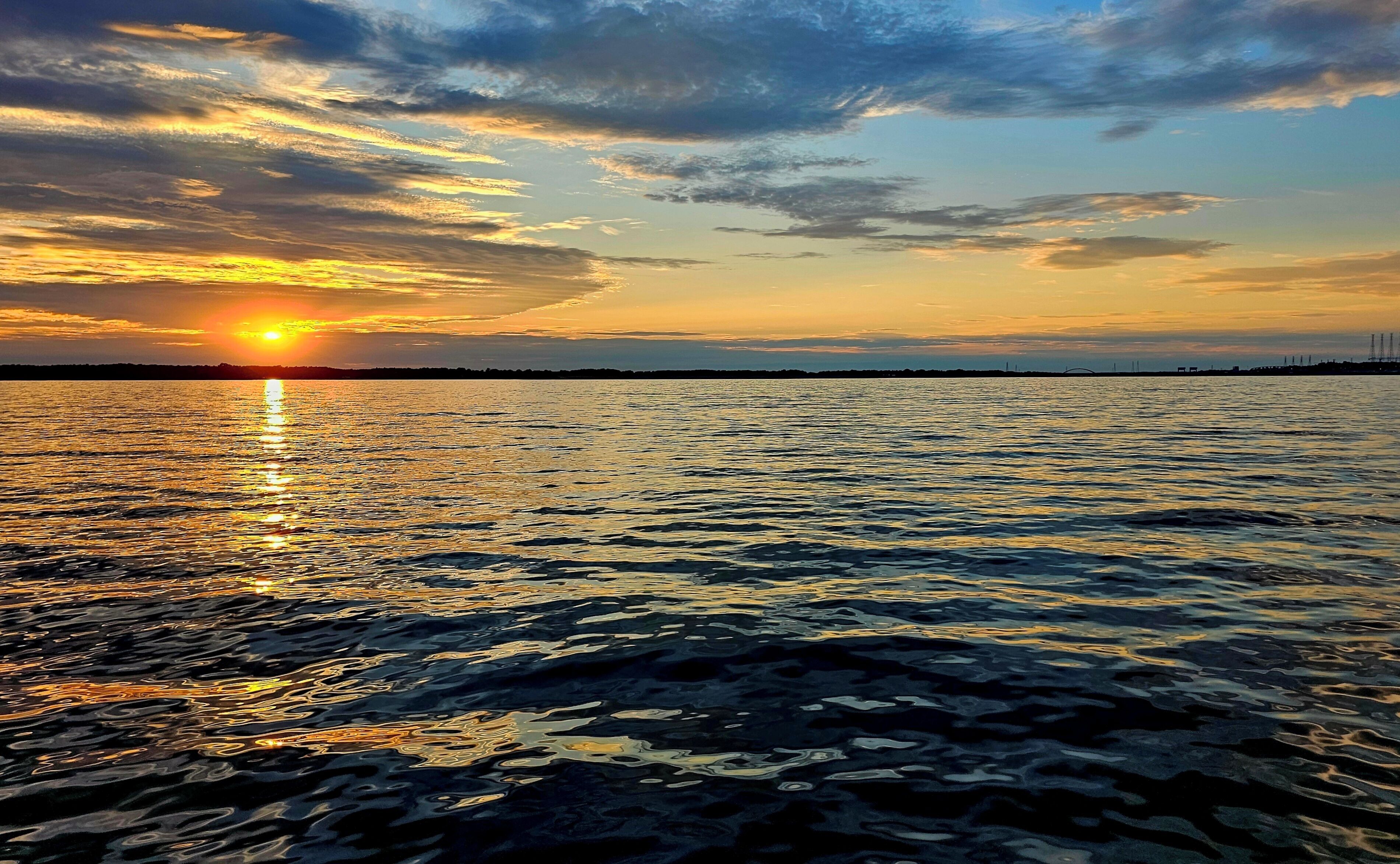 A sunset over a calm body of water with a distant shoreline and a bridge.