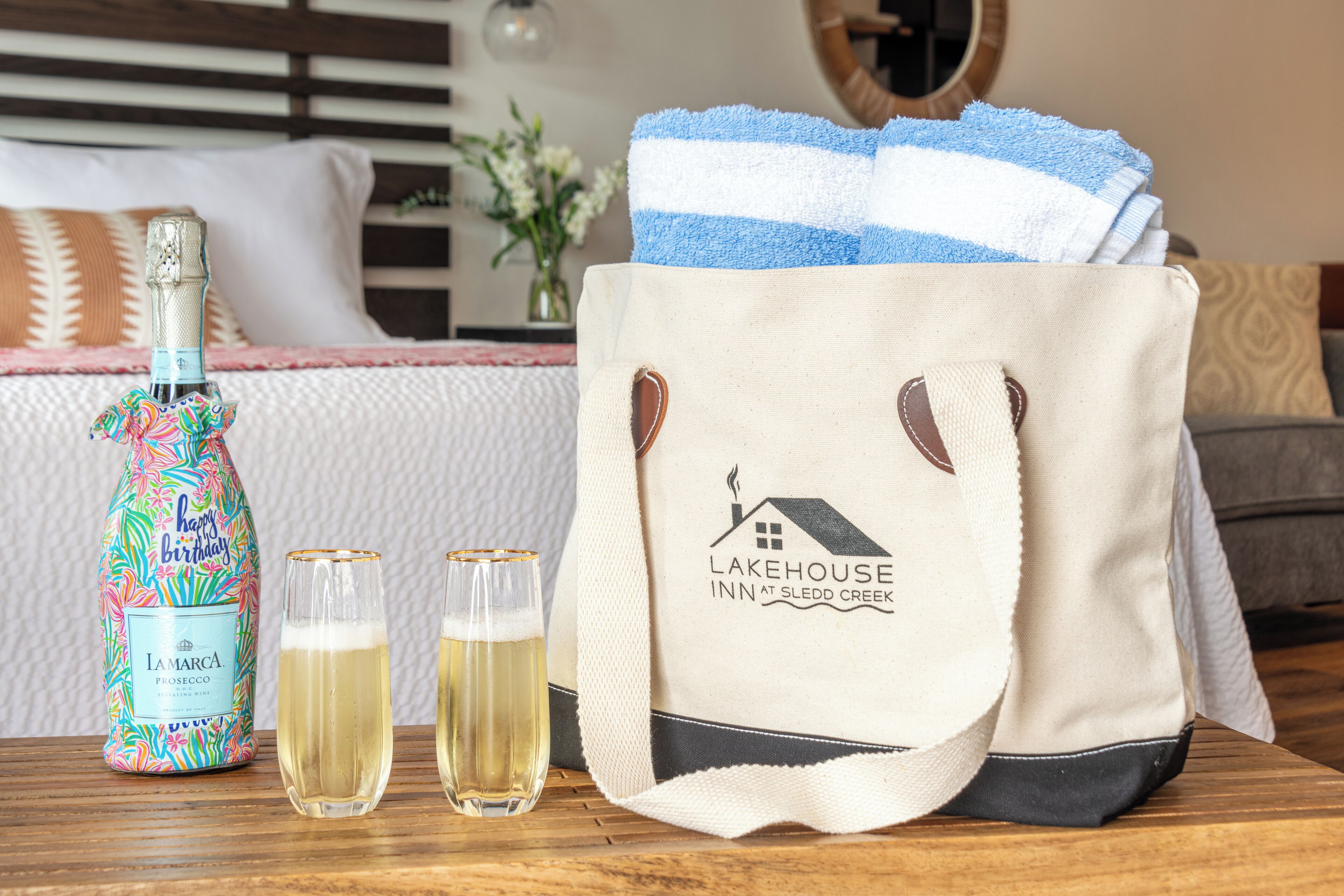 A bottle of La Marca Prosecco, two glasses of wine, and a tote bag with the Lakehouse Inn at Sledd Creek logo.