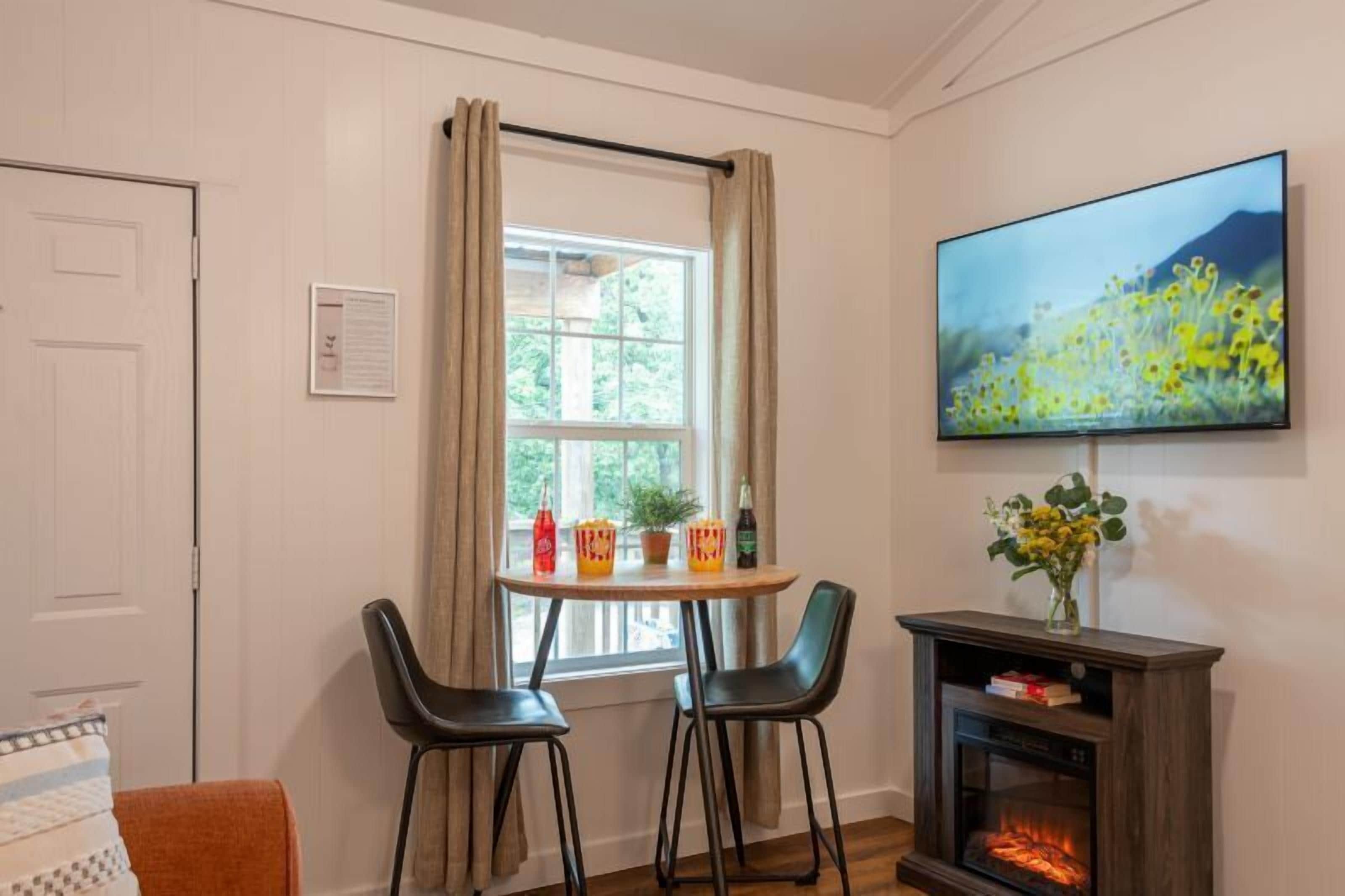 A cozy room with a dining table, two chairs, a TV mounted on the wall, and a fireplace.