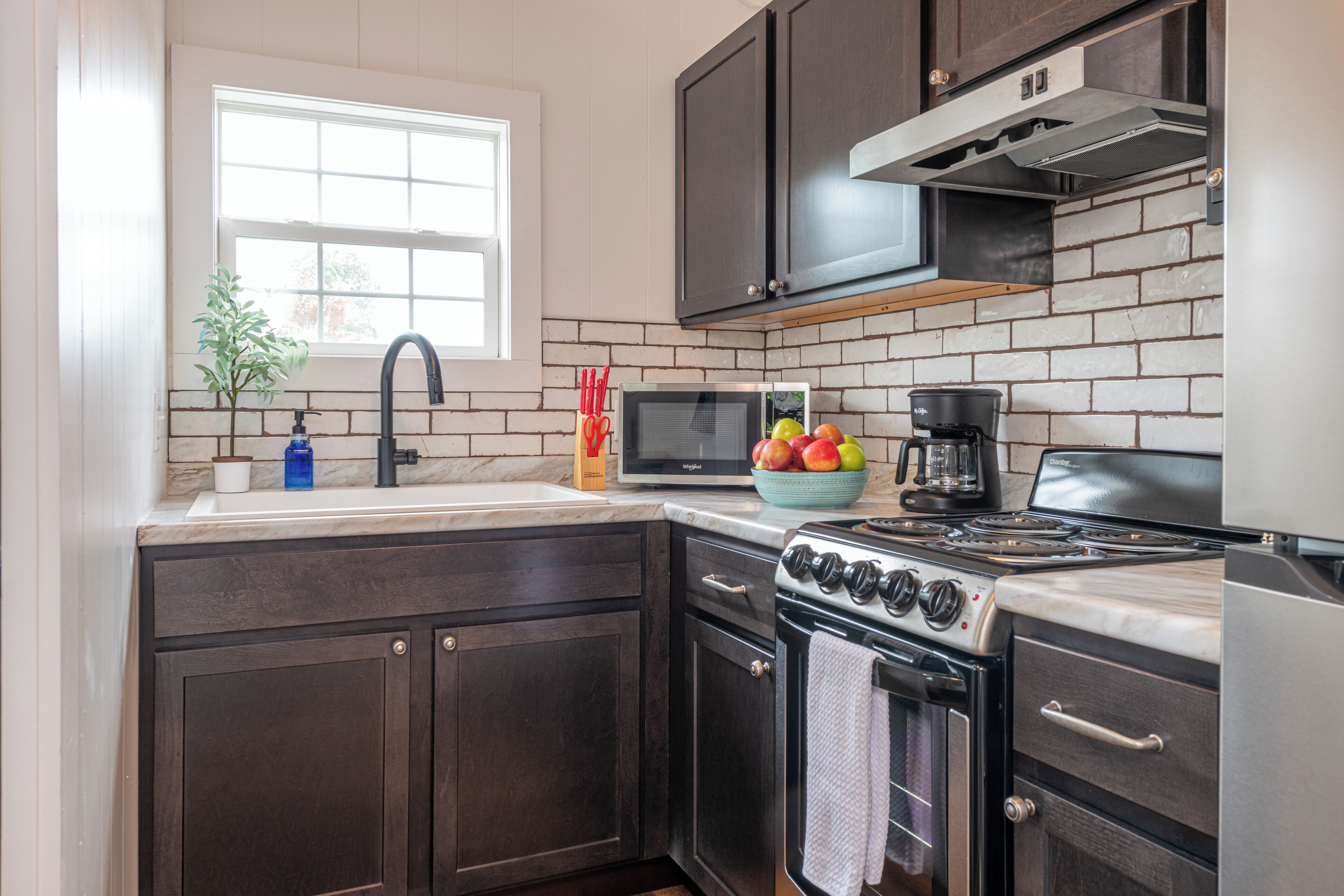 A kitchen with dark wooden cabinets, a black stove, a microwave, and a window above the sink.