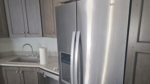 Un refrigerador Whirlpool de acero inoxidable en una cocina con gabinetes de madera y piso de baldosas.