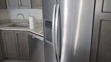 A stainless steel Whirlpool refrigerator in a kitchen with wooden cabinets and a tiled floor.