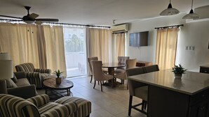 Un salón con sofás a rayas, una mesa de comedor y una zona de cocina con televisor.