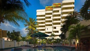 Un hotel con piscina, palmeras y un edificio de varios pisos con balcones.