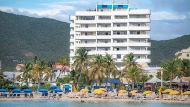 Un hotel de varios pisos con balcones, una playa en primer plano y palmeras.