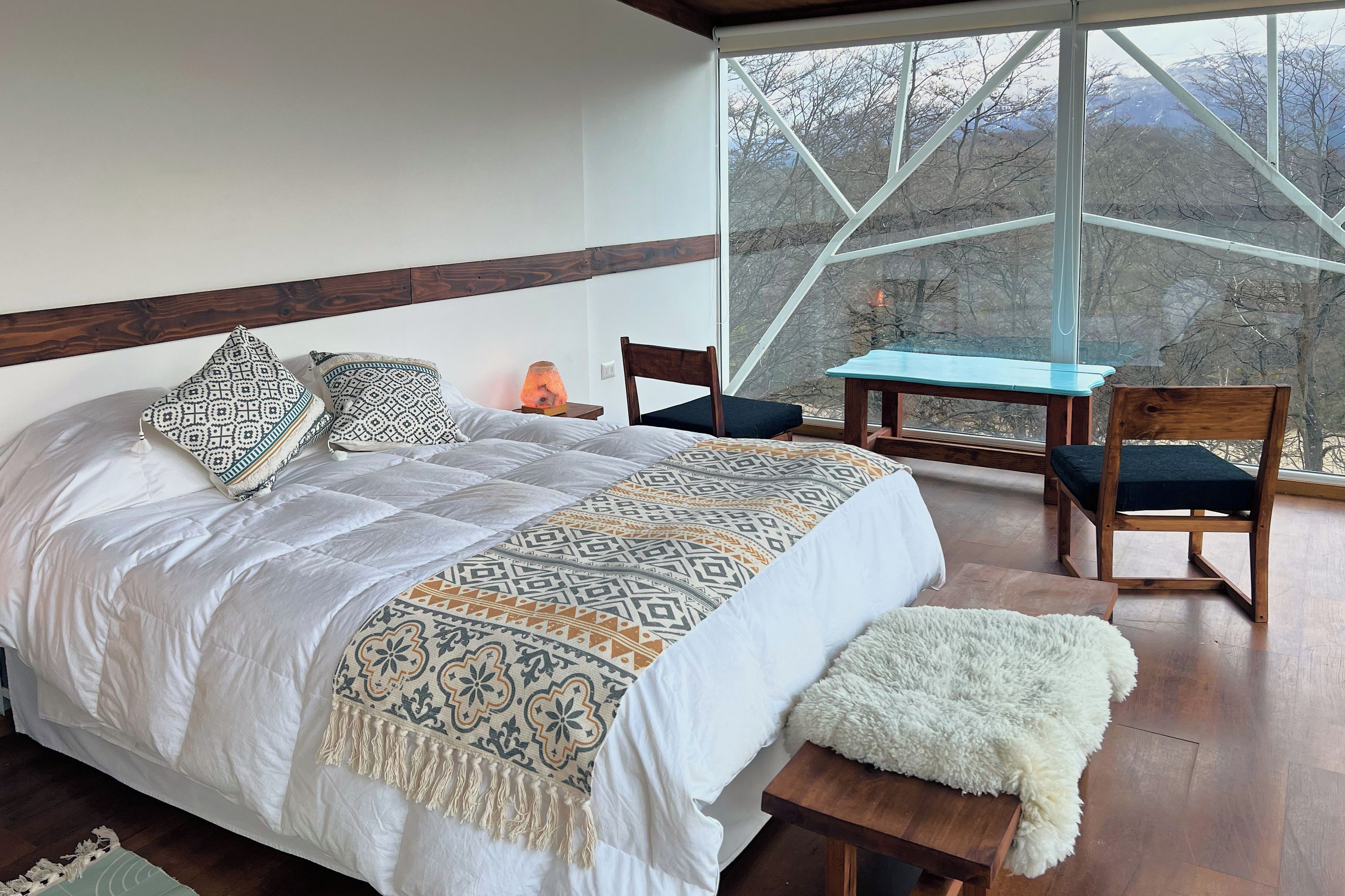 Un dormitorio con una cama grande, una silla, una mesita y vistas al exterior a través de un ventanal.