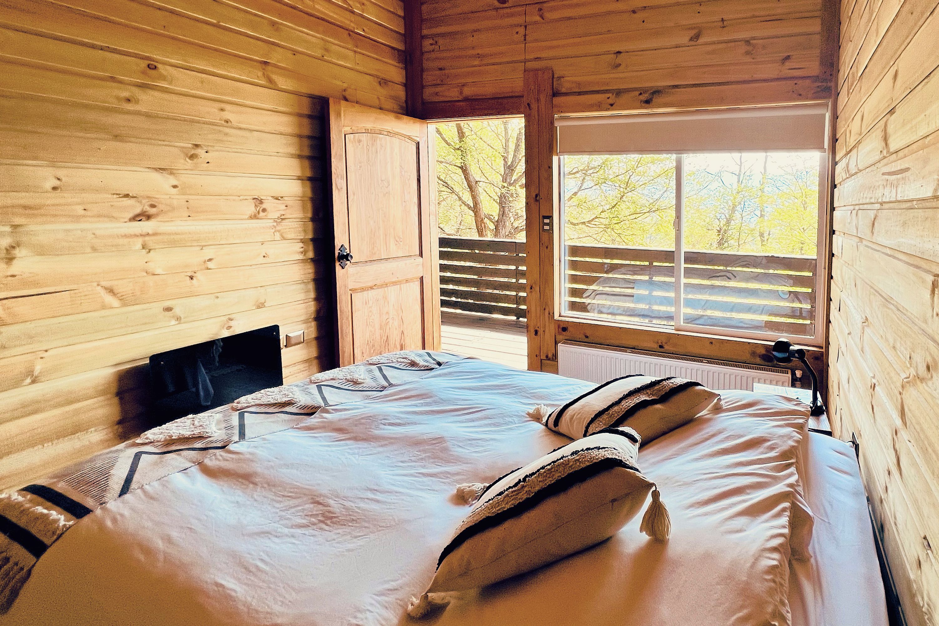Ein Zimmer einer Holzhütte mit einem Bett, einem Fenster und einer Tür.