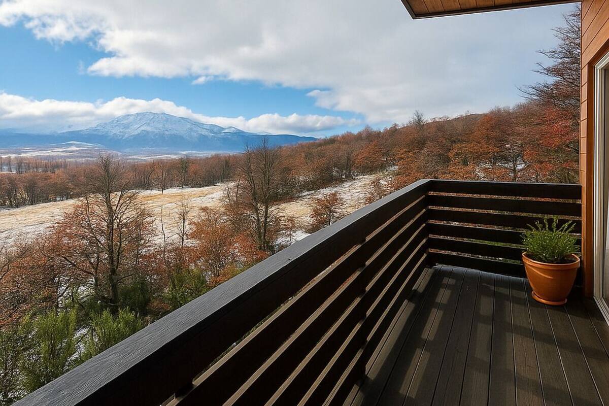 Una terraza de madera con vista a una montaña nevada y follaje otoñal.