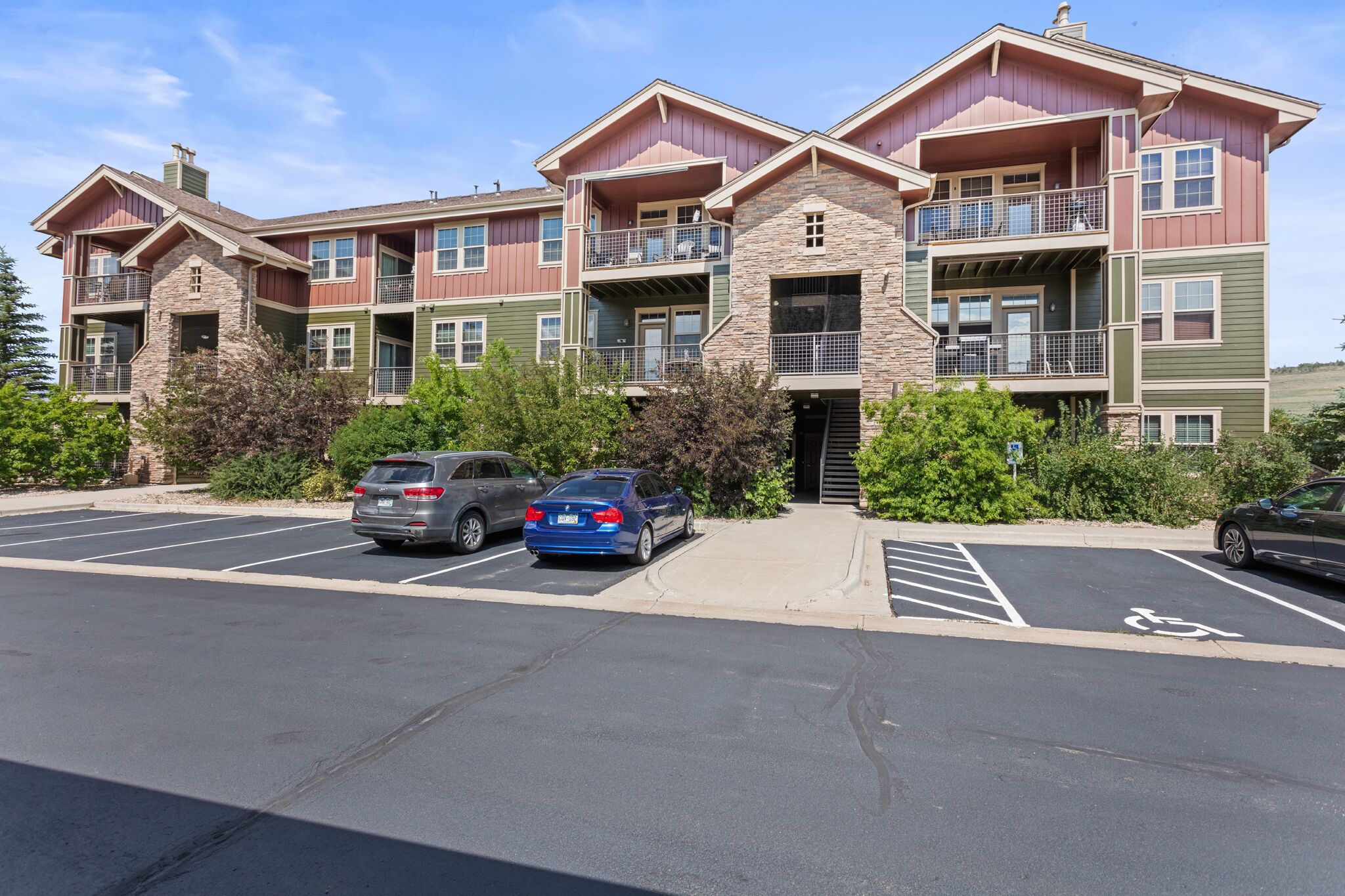 A multi-story residential building with balconies, a parking lot, and a clear sky.
