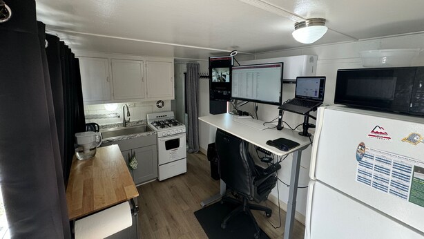 A compact kitchen with a stove, sink, and refrigerator, a desk with a computer and a laptop, and a microwave. - Midtown Charm: 1BR Urban Pad (Reno)