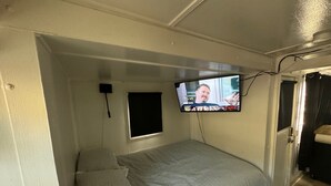 A small, single-bed room with a television mounted on the wall, a window, and a door. - Midtown Charm: 1BR Urban Pad (Reno)