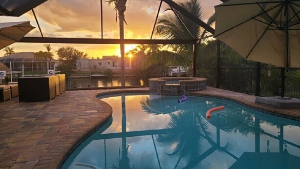 Una piscina con vista al atardecer, rodeada de palmeras y un patio de ladrillo.