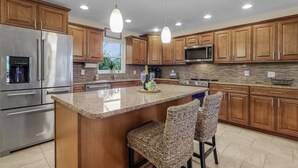 Una cocina moderna con armarios de madera, electrodomésticos de acero inoxidable y una isla central con taburetes de bar.