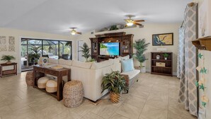 Un salón amplio con un televisor grande, ventiladores de techo y un espacio de estar cómodo.
