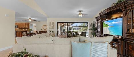 A living room with a large sectional sofa, a flat-screen TV, and a ceiling fan.