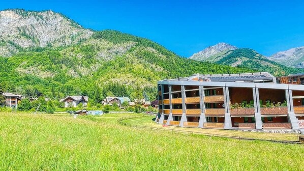 A modern building with multiple balconies, surrounded by a lush green landscape and mountains.