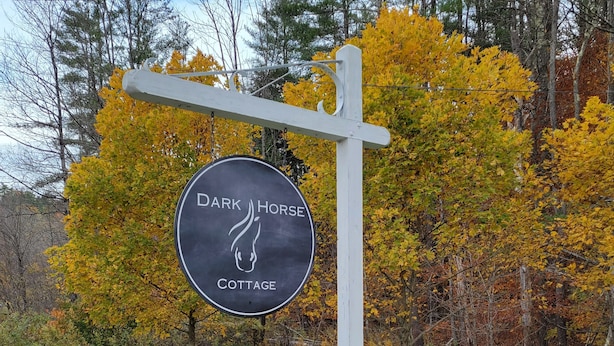 Un panneau indiquant l’emplacement de « Dark Horse Cottage », avec un poteau blanc et un panneau circulaire.