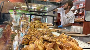 Una vitrina de panadería con diversos tipos de pasteles, incluyendo croissants y pan, en una tienda bien iluminada.