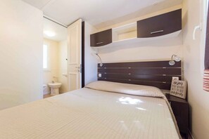 A bedroom with a bed, a bedside table, a nightstand, a wall-mounted shelf, a window, and a door. - Mobilehome with terrace, air conditioning and pool (Fondotoce di Verbania)