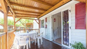 Un espacio al aire libre techado con una terraza de madera, una mesa con sillas y un ventanal corredero que da a una habitación.