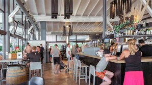 Un bar interior con techo alto, ventanas amplias y una barra con taburetes.