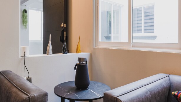 A modern living room with a sofa, a small round table, and a large window with blinds.