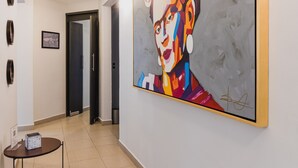 A hallway with a large abstract painting on the wall, a round table with a box, and a door at the end.