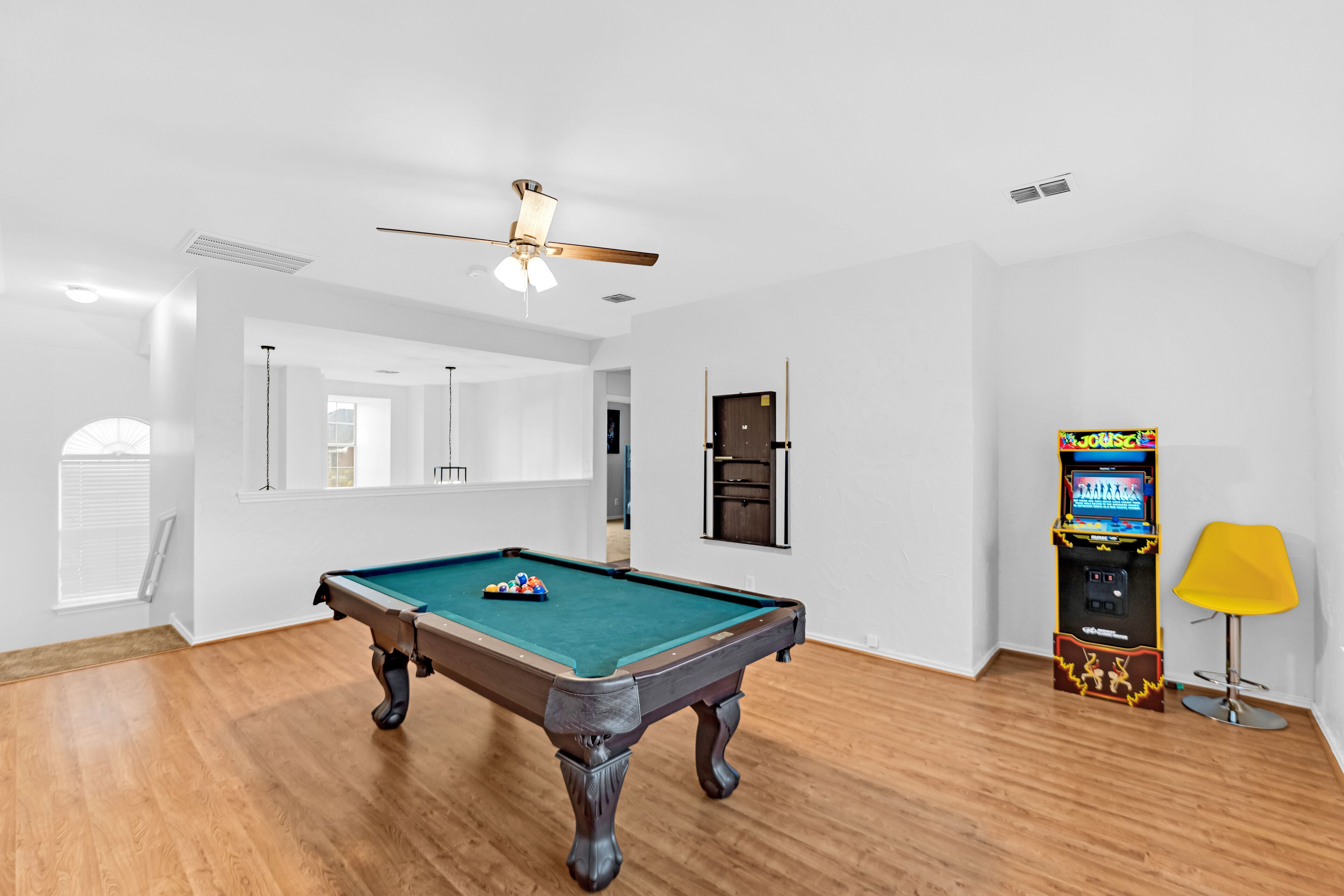 A pool table in a room with wooden flooring, a ceiling fan, and a jukebox.