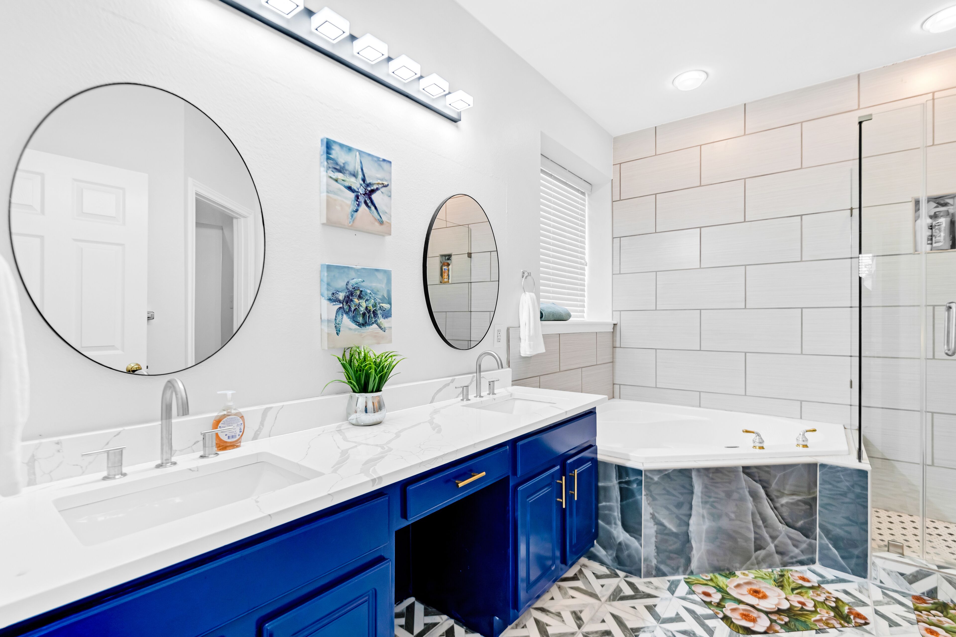 Un baño moderno con tocador blanco, dos lavamanos, armarios azules y zona de ducha.