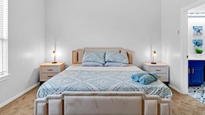 Une chambre à coucher comprenant un lit, deux tables de chevet, une commode, une fenêtre avec des stores et une armoire bleue.