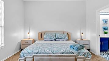 Quarto com uma cama, duas mesas de cabeceira, um criado-mudo, uma janela com persianas e um armário azul.