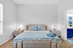 A bedroom with a bed, two bedside tables, a nightstand, a window with blinds, and a blue cabinet.