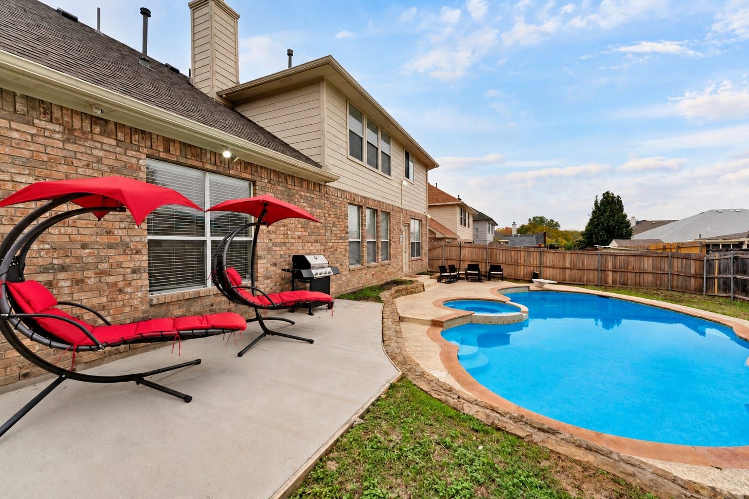 A backyard with a swimming pool, a brick house, and outdoor seating with umbrellas.