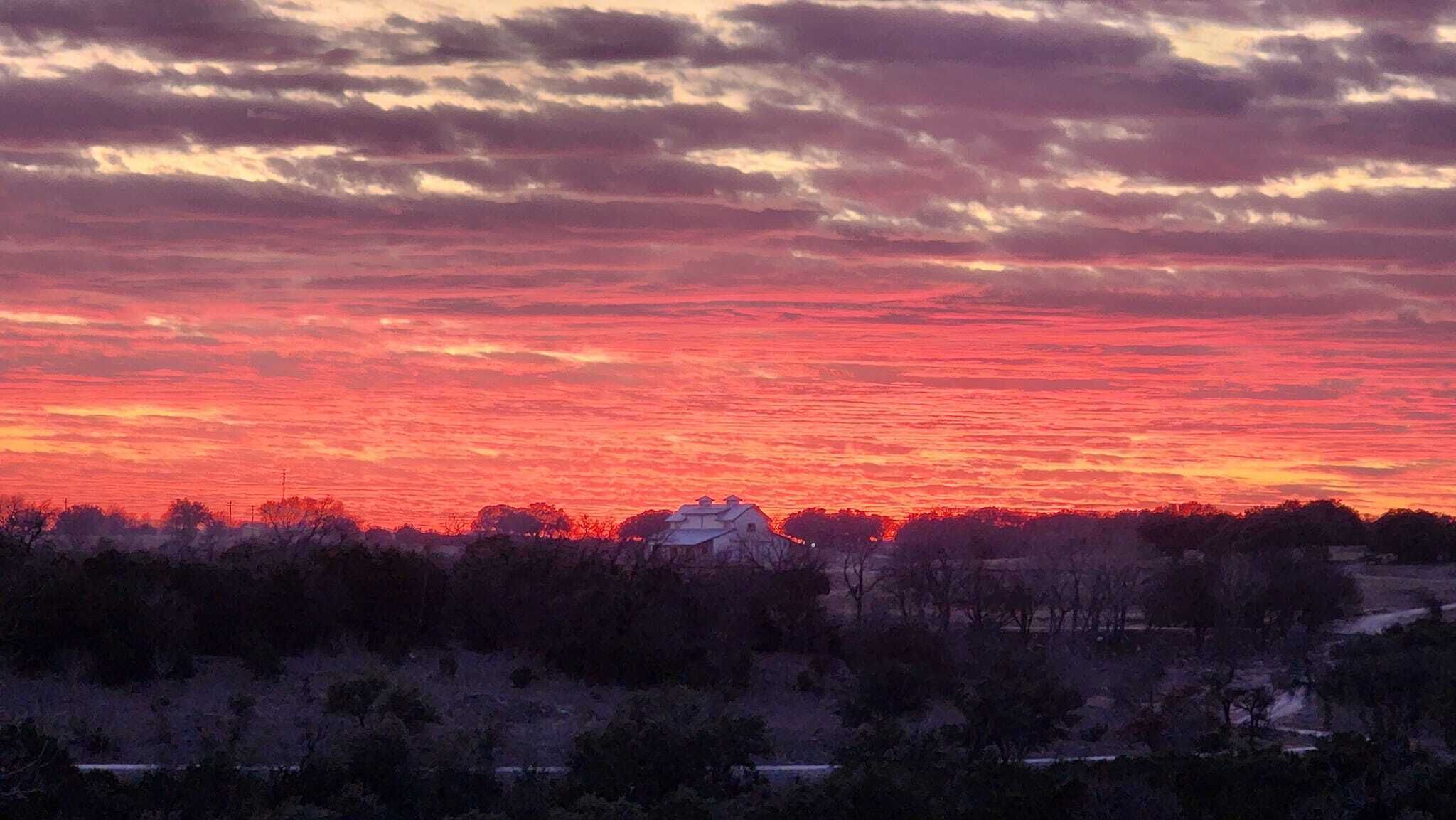 A sunset over a rural landscape with a house in the foreground.