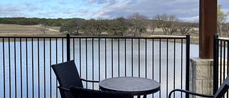 A balcony with a round table and two chairs, overlooking a body of water with a metal railing.