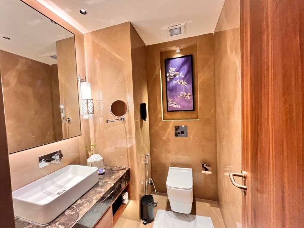 Een moderne badkamer met een grote spiegel, een witte wastafel, een toilet en een kunstwerk in een lijst aan de muur.