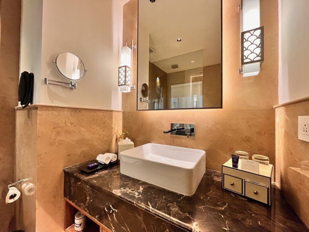 Une salle de bain avec un grand miroir, un lavabo rectangulaire et un comptoir en marbre.